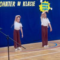 Dziewczynki biorące udział w akademii wykonują układ choreograficzny do nowoczesnej muzyki. Ubrane są w luźne stroje.